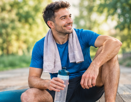 Un sportif après sa séance, assis dans un espace extérieur, avec une bouteille d'eau, dans une attitude détendue.